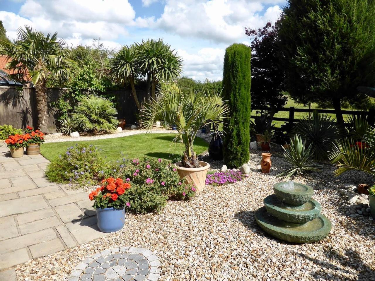 Gravel garden with palms, ornamental grasses and a stone water feature