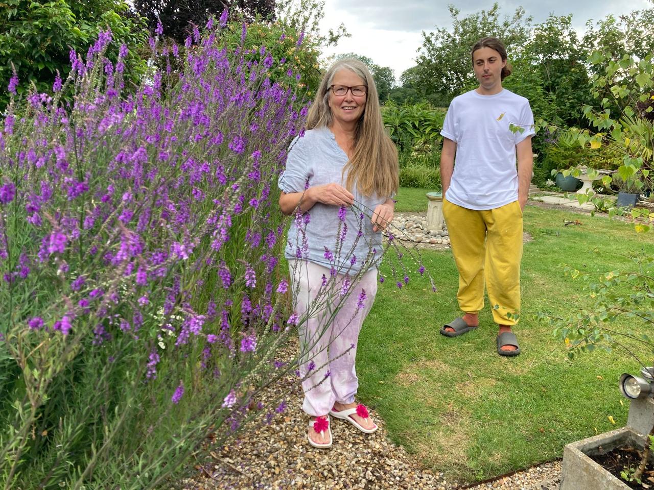 Two visitors beside a tall border of purple flowers