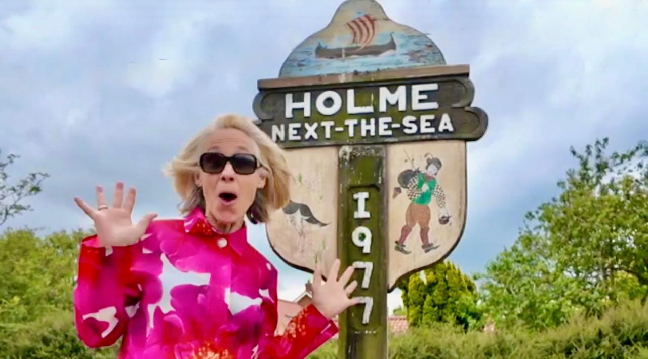 A visitor posing playfully at the Holme-next-the-Sea village sign