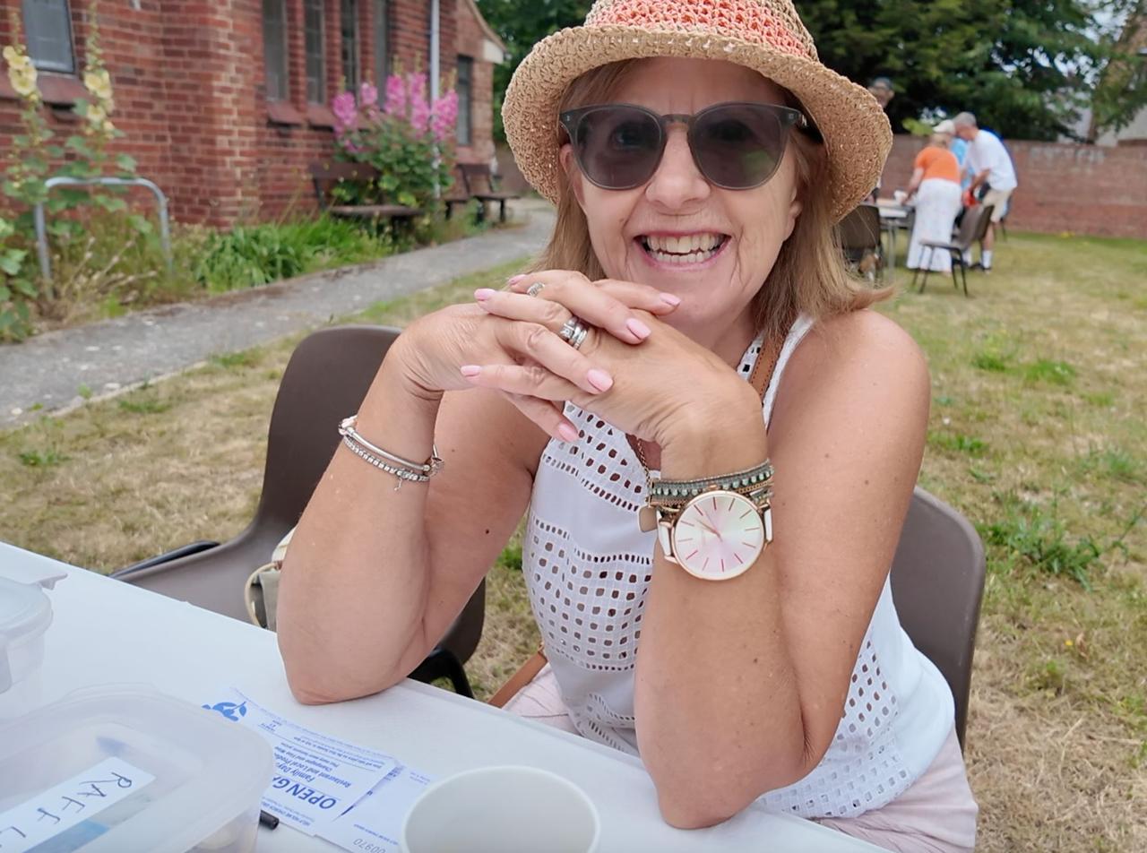 A smiling visitor in a straw hat at an outdoor table