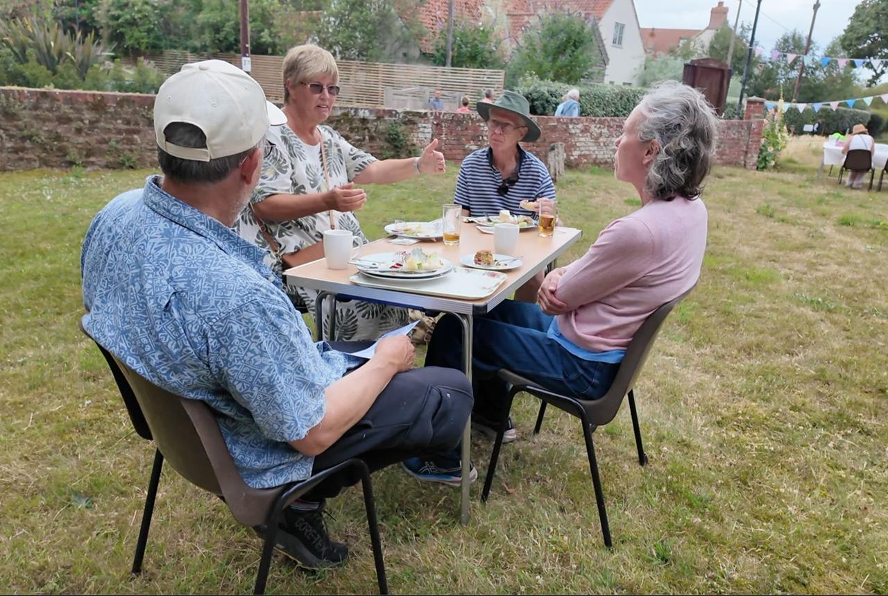 Four visitors sharing refreshments at a table on the grass