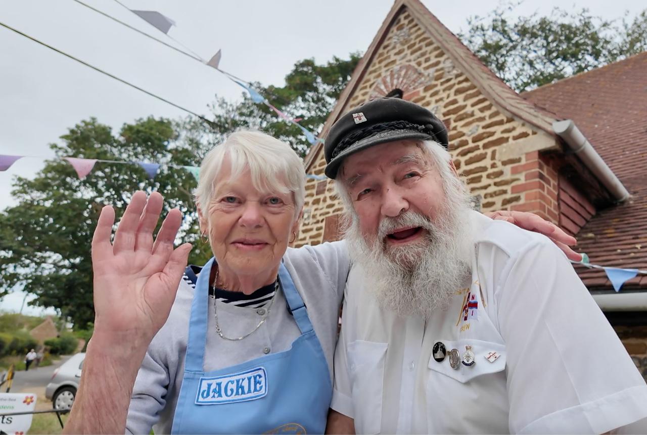 A volunteer named Jackie waving beside Geoff in a sailor cap