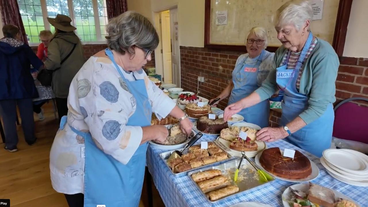 Volunteers serving from a table laden with cakes in the Village Hall
