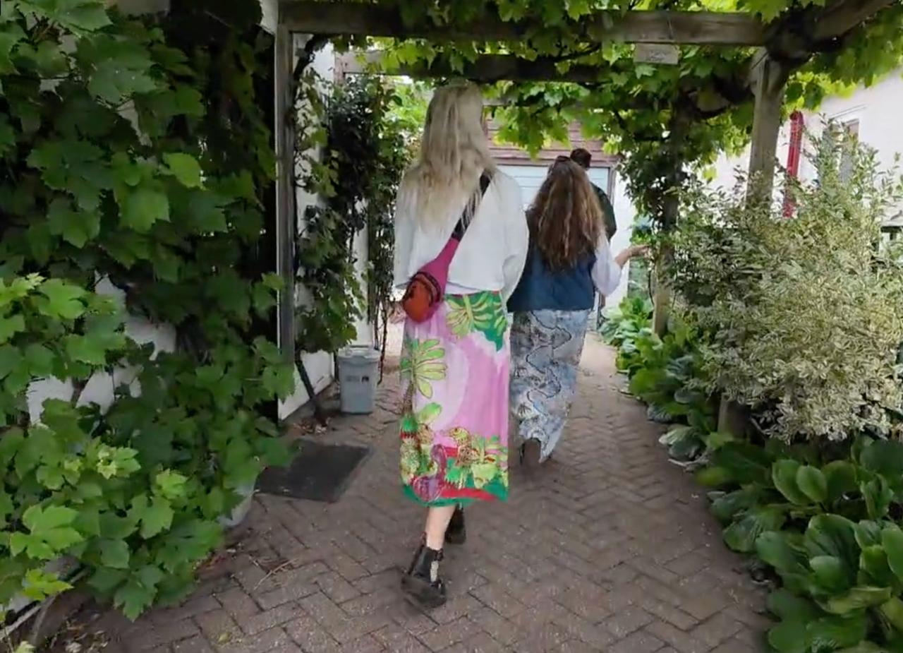 Two visitors walking beneath a vine-covered pergola walkway