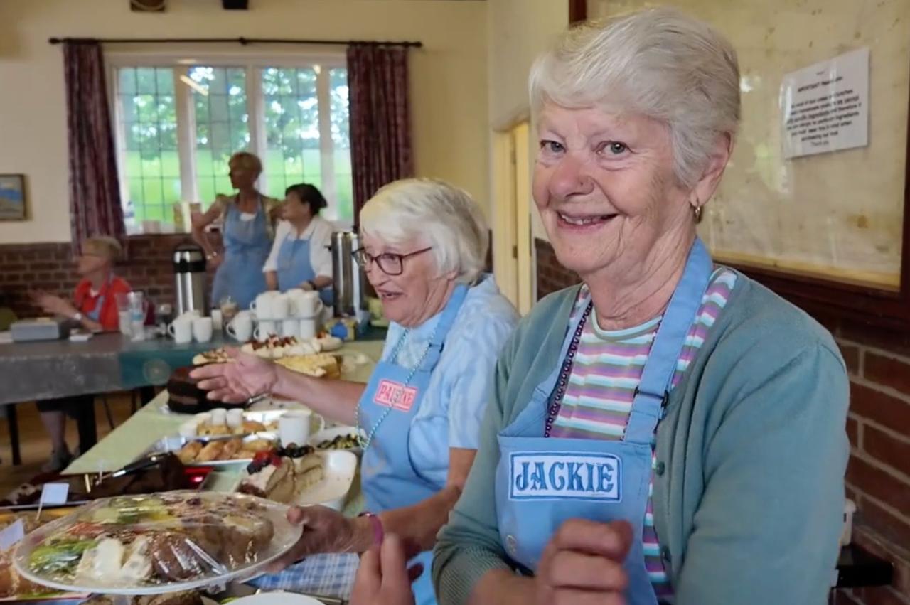 Smiling volunteers serving cakes in the Village Hall