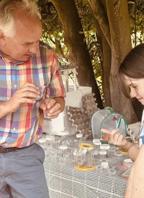 A girl studying a moth on her hand while the moth expert explains, at a table of specimen pots